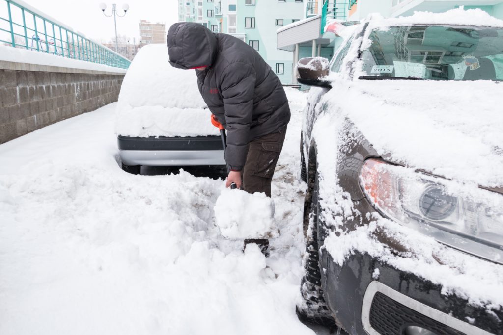 Homem tirando a neve do carro com uma pá