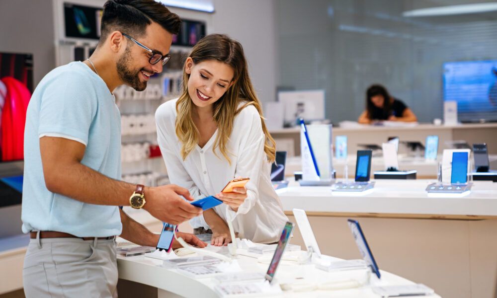 Um casal jovem em uma loja de telefones analisando um telefone para comprar